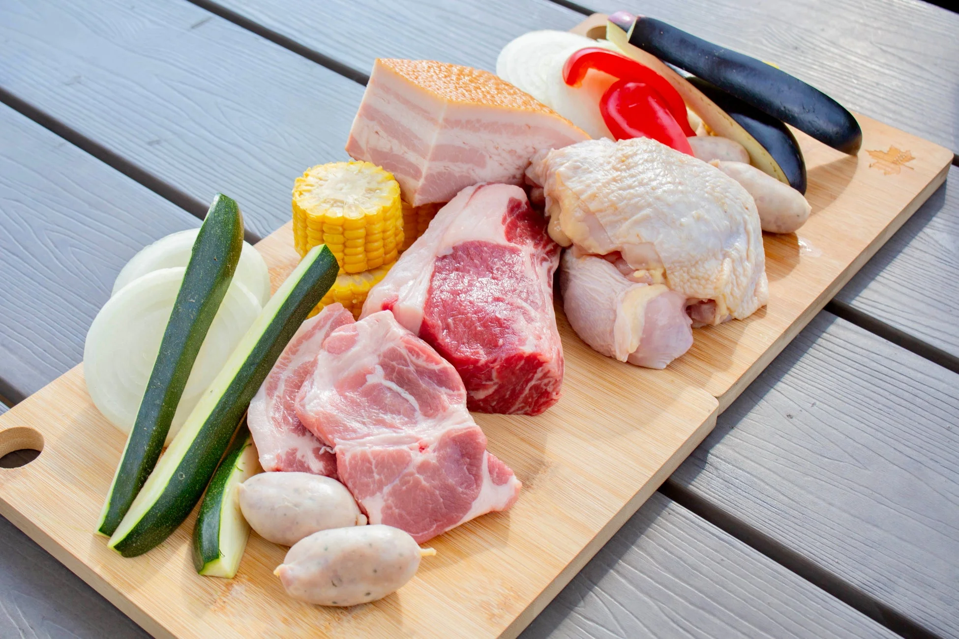 バーベキュー用の様々な生肉と野菜が木製のまな板にきれいに盛り付けられている