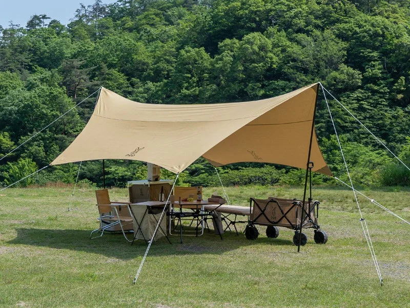 緑豊かな森を背景にした広々とした芝生の上で、ベージュ色の大きなタープが日差しを遮っています。