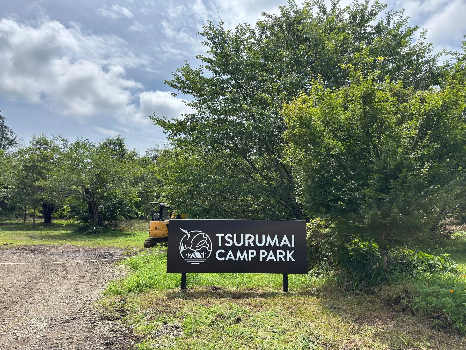 「TSURUMAI CAMP PARK」と書かれた看板が立つ、自然豊かな場所の入り口の風景。