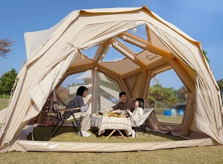 晴れた日に広々としたテントの中で、家族3人がテーブルを囲んで食事や会話を楽しんでいる様子。アウトドアでのんびり過ごす休日の風景です。