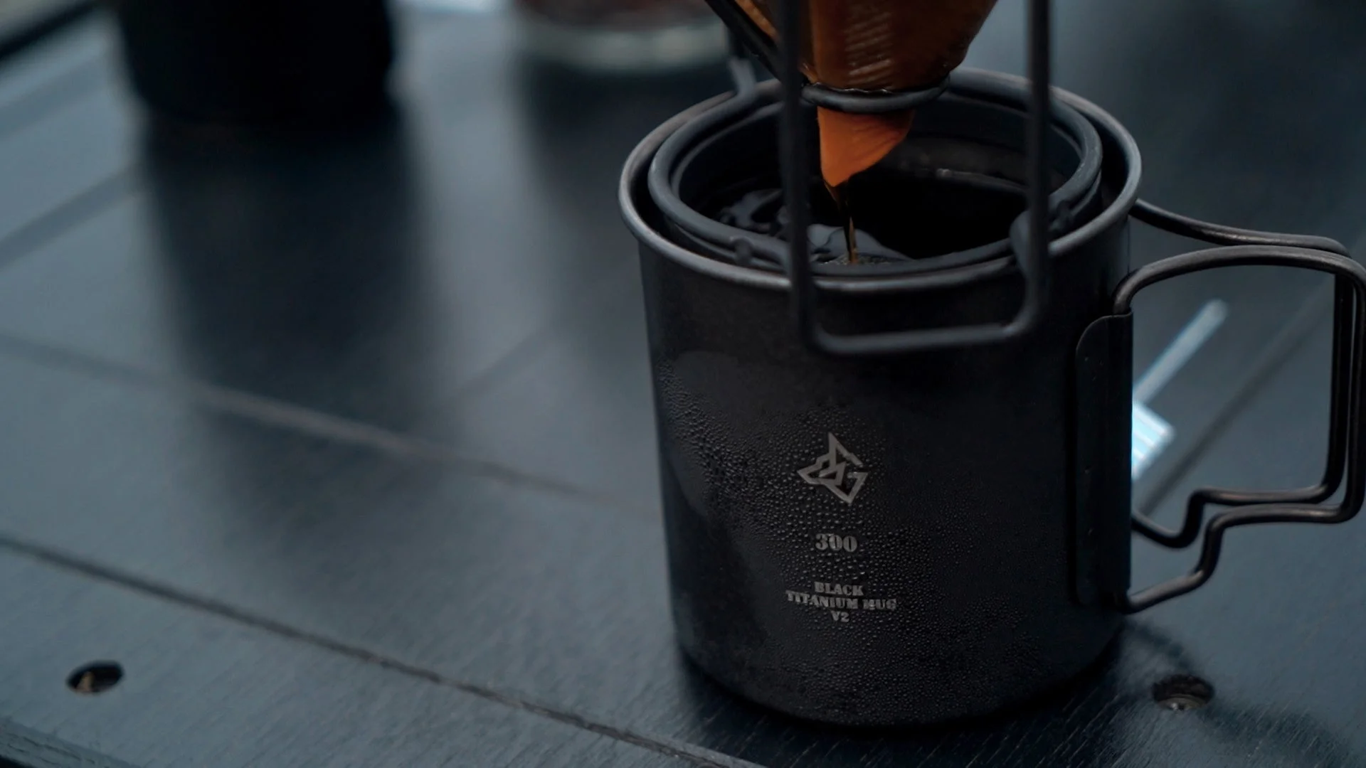黒いチタン製マグカップにコーヒーが注がれている様子を捉えた画像です。