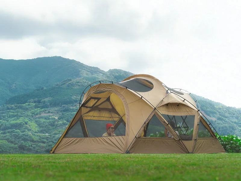 緑豊かな山々を背景に、広々としたベージュのドーム型テントが草地に設営されています
