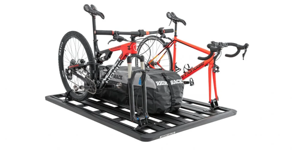 2台の自転車（マウンテンバイクとロードバイク）と大型の防水バッグが搭載されたルーフラックシステムの画像です。アウトドア用品の運搬ソリューションを示しています。