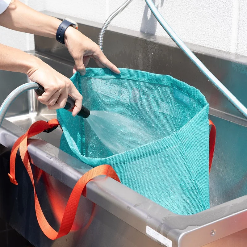 屋外のシンクでメッシュバッグに水を注いでいる様子