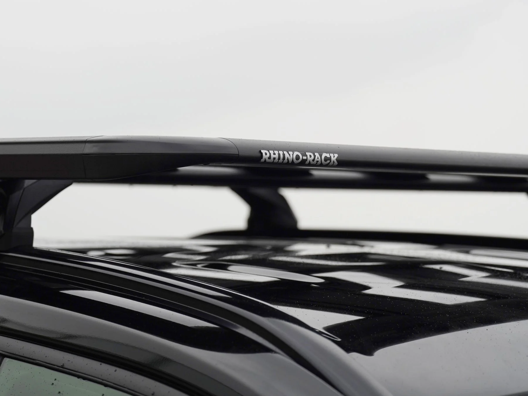 黒い車の屋根に設置された「RHINO-RACK」ブランドのルーフラックがクローズアップで写っています。