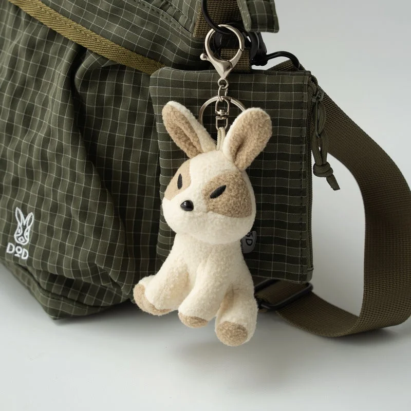 カーキ色のチェック柄バッグに、DODのロゴと、白と茶色のぶち模様のうさぎのぬいぐるみキーホルダーが取り付けられています