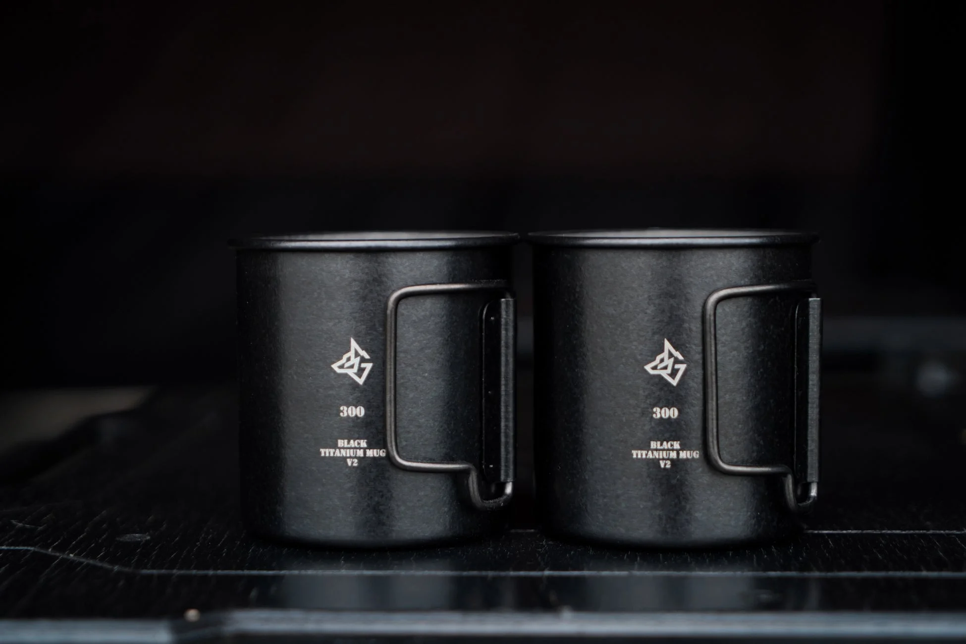 黒い背景に置かれた2つの黒いチタン製マグカップが写っています。